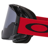 Oakley Airbrake goggles with a black frame and dark tinted lens, featuring a bright red elastic strap with a black Oakley logo, shown on a white background.